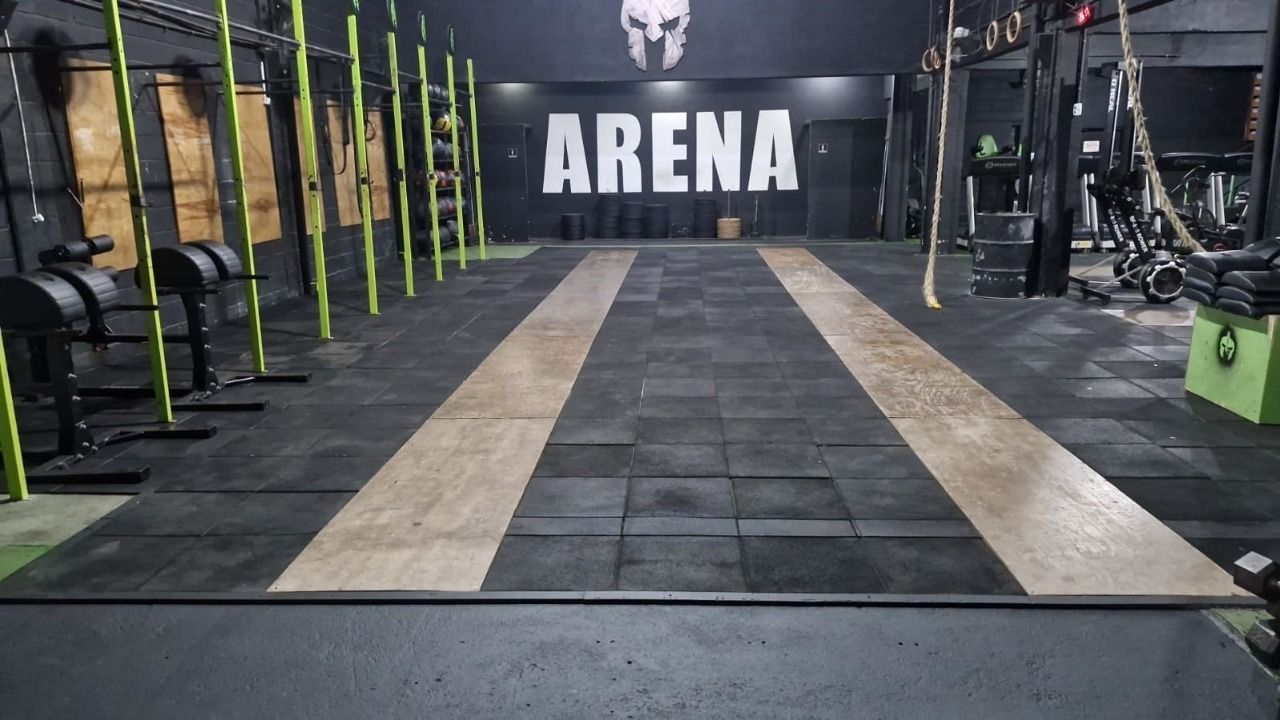 O salão de treino da Cross Arena, com plataformas, estruturas verdes e o letreiro ARENA ao fundo