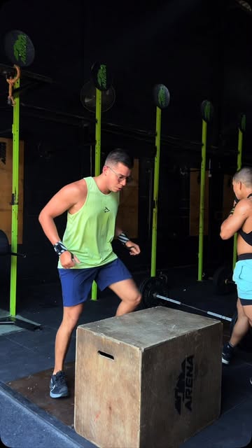 Aluno de camiseta verde treinando próximo a uma caixa e às estruturas do box
